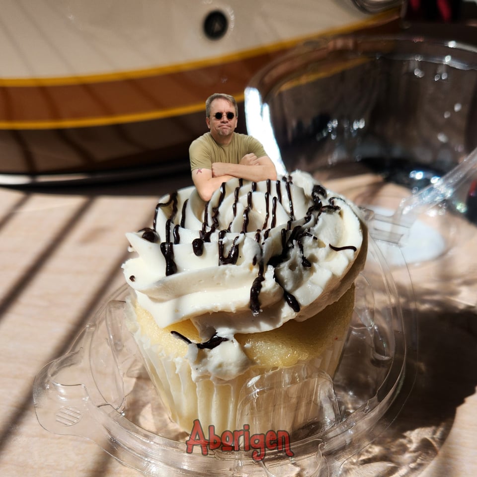 A tiny Aborigen rests his elbows in the icing of a salted caramel cupcake.