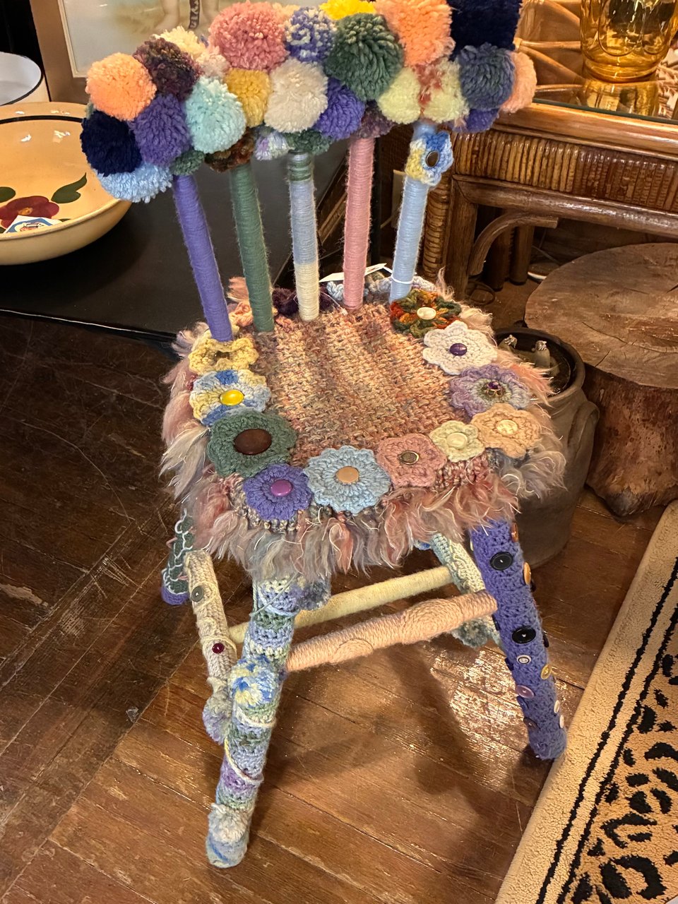 A chair festooned with crocheted nonsense and pom-poms.