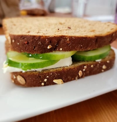 A cucumber sandwich on wheat bread with cream cheese and honey on a white plate