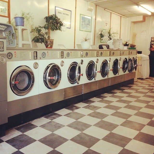 The interior of a launderette with a row of washing machines and a chequered linoleum floor.