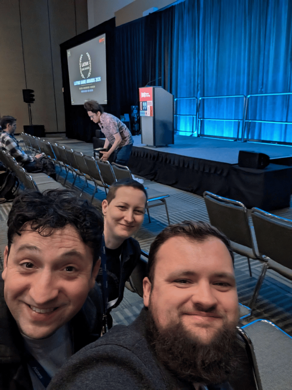 Jess, Adam Riches, and Joseph Riches posing for a selfie in front of the stage for the Latinx Game Awards