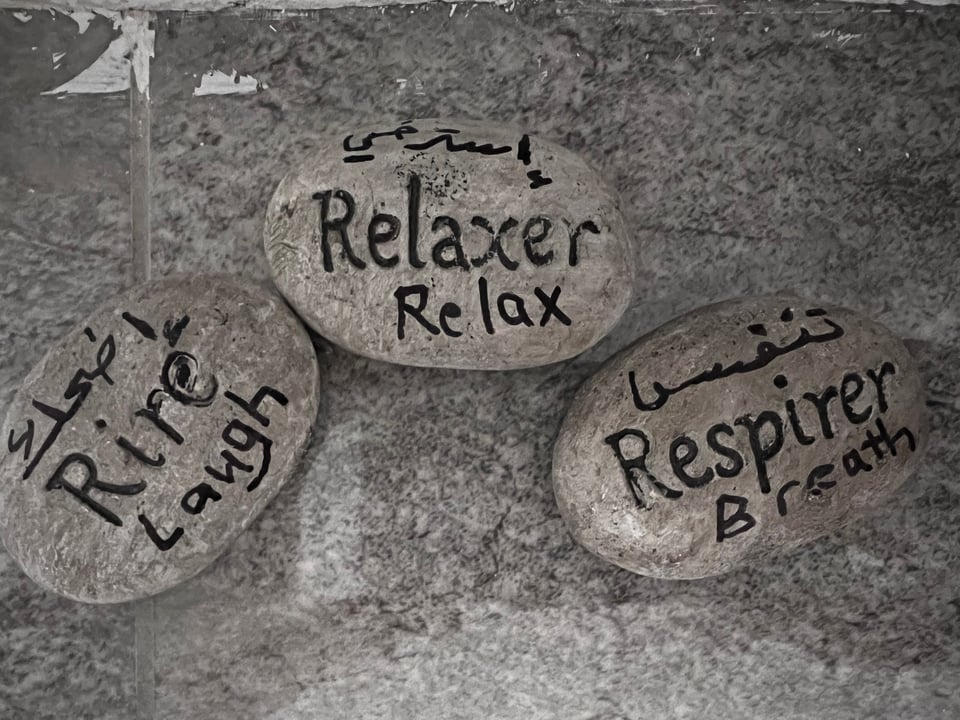 Three smooth stones with the words laugh, relax, and breathe, written in Arabic, French, and English