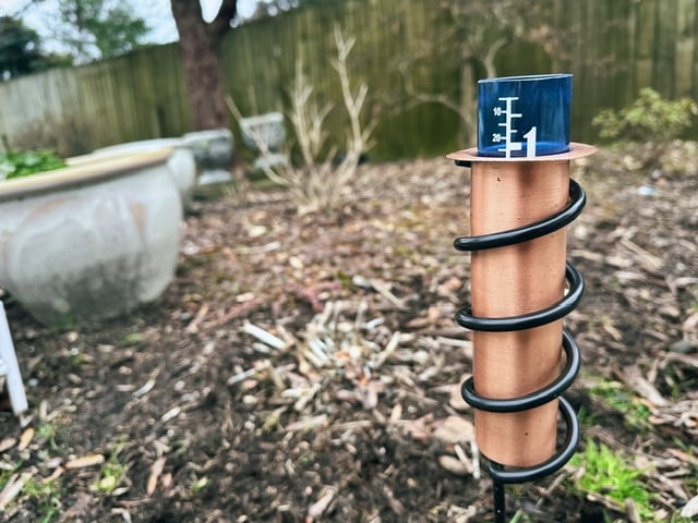 A blue rain gauge in a copper tube. It says about an inch of rain fell yesterday, which, idk, seems like a lot.
