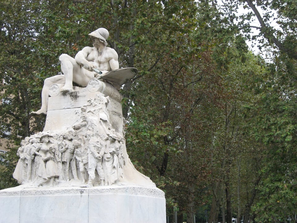 photo of Monument to Felice Cavallotti in Milan by Ernesto Bazzaro, showing a naked recumbent statue between of Spartan king Leonidas between two sculpted pillows, with scenes from Cavallotti's life carve into the base below