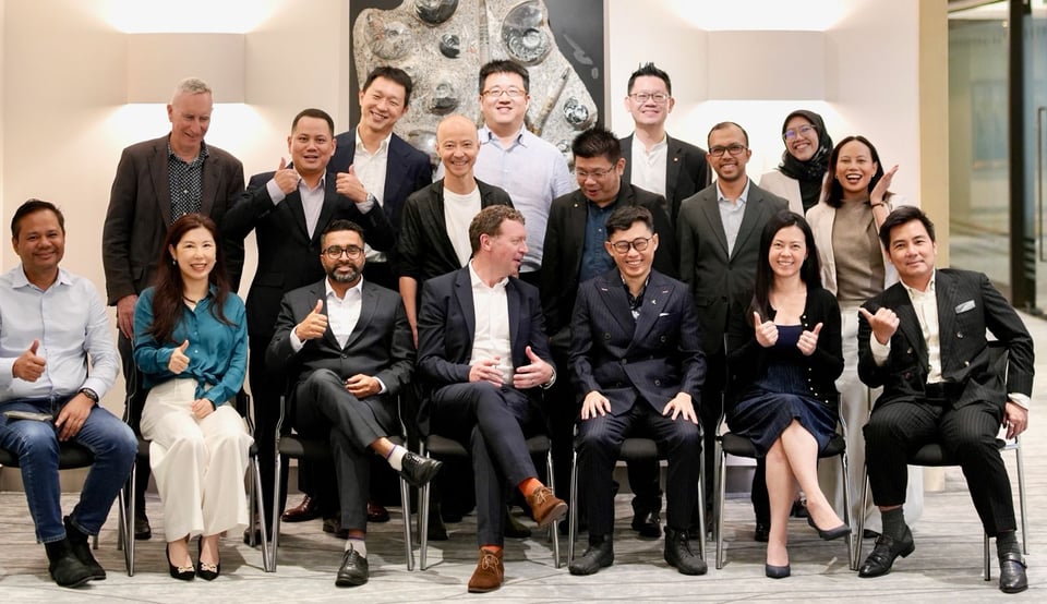 Seventeen people in suits (mostly) posing informally for a group photo. Some have raised thumbs. Mikail Jaman has both thumbs raised.