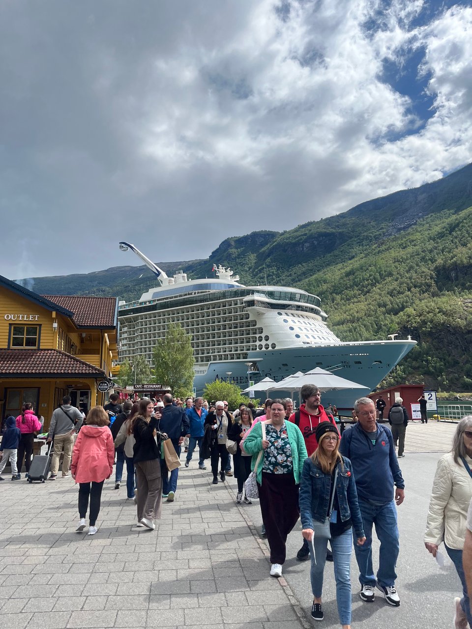 Tourists walking in front of large cruise ship that is almost as tall as fjord