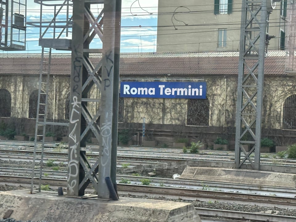 Photo of train tracks and scaffolding, with a sign that reads "Roma Termini" on a low building