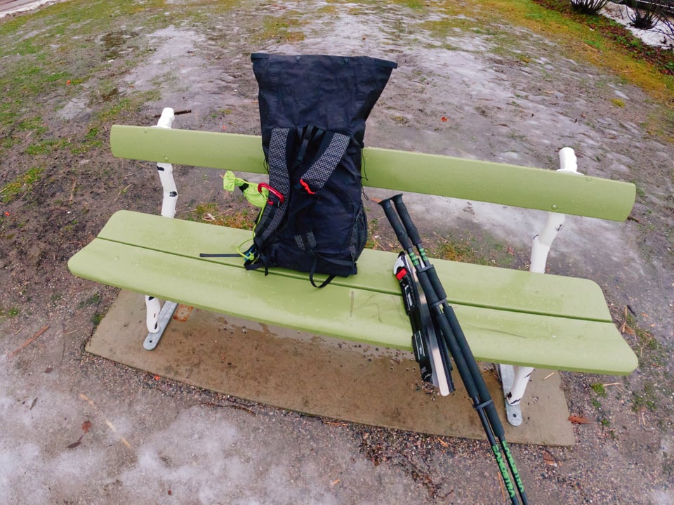 A backpack, a pair of skates, and a pair of poles on a bench in a park.