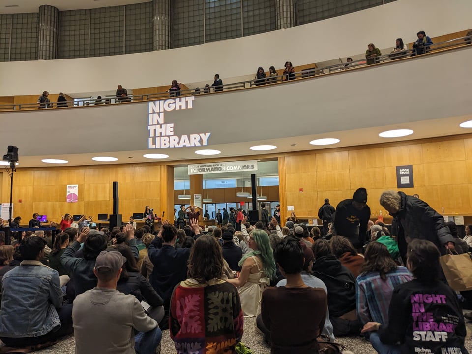 dozens of people sitting cross-legged on the floor of the grand lobby in the Brooklyn Public Library Central branch doing a meditation session.