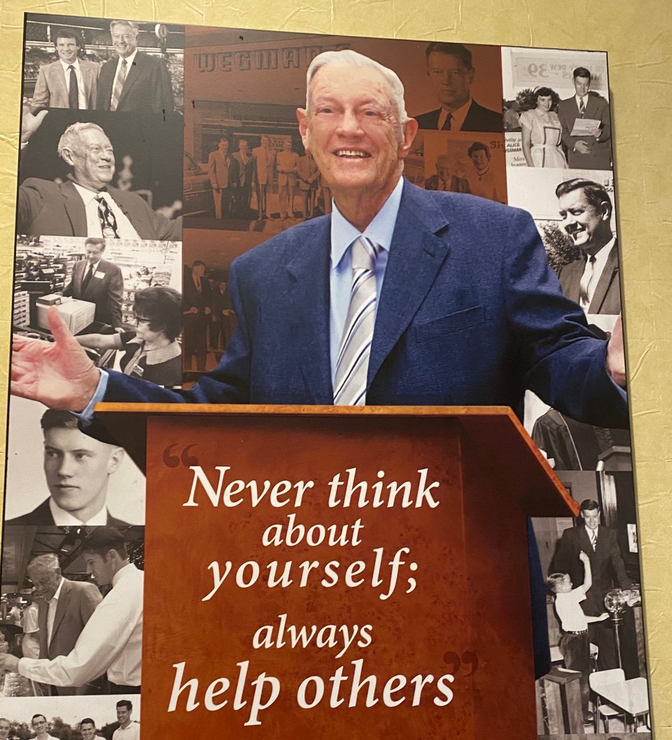 A photo of a man at a podium. The sign on the podium says "Never thing about yourself; always help others"