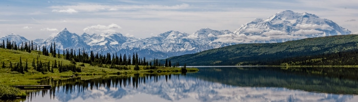 An image of a snow-covered mountain range with a lake and green trees in front of it