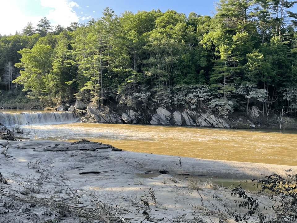 Flooded river and waterfall. In the background you can see the high water mark in the trees and in the foreground there's a lot of sand.
