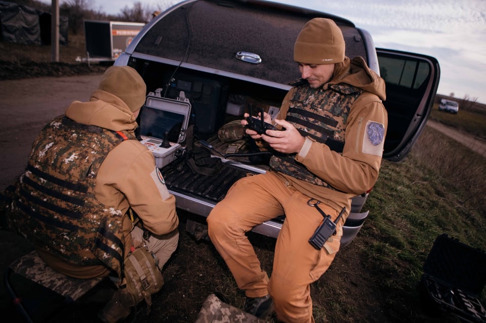 Two members of the demining team work with drone remotes from the back of a truck