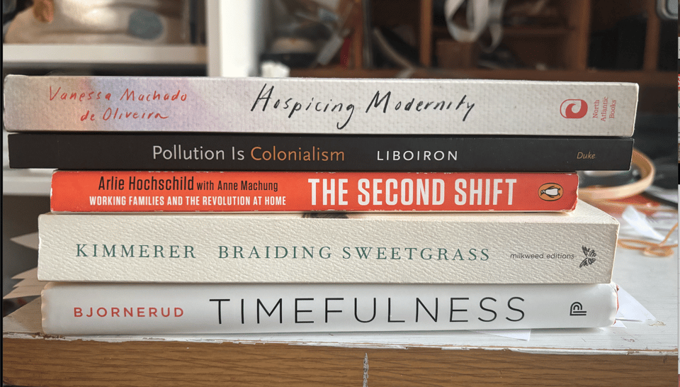 A stack of books on a desk: Hospicing Modernity, by Vanessa Machado de Oliveira; Pollution is Colonialism by Max Liboiron; The Second Shift by Arlie Hochschild; Braiding Sweetgrass by Robin Wall Kimmerer; Timefulness by Marcia Bjornerud