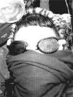 black and white photo of a person with dark bangs, swimming goggles, and a scarf over her nose and mouth. On her head is a cheetah print hat with ears.