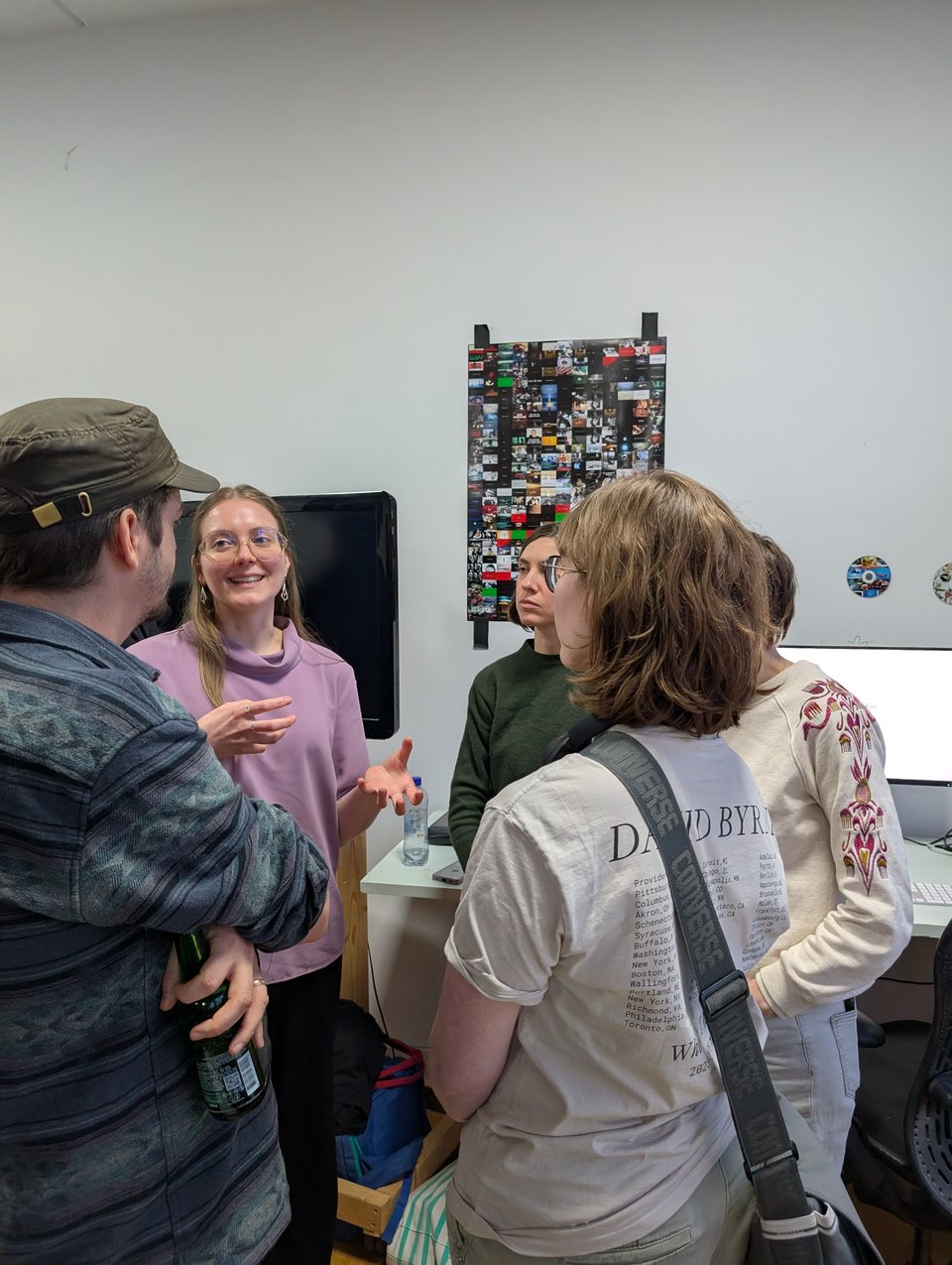 A group of people chatting. One, with back facing the camera, is wearing a David Byrne tshirt.