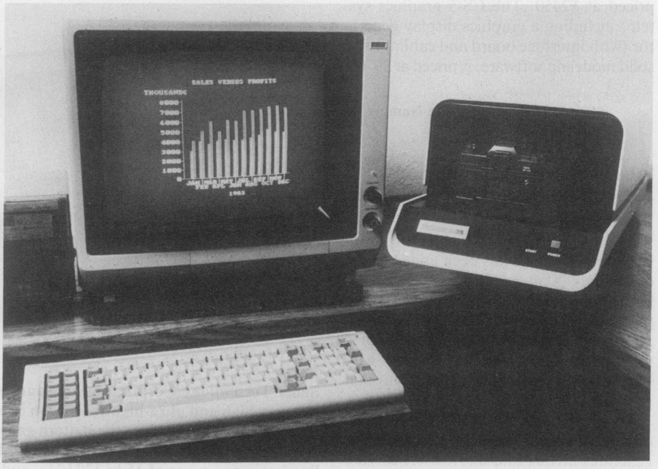 A black-and-white image of the VideoSlide35 sitting on a desk next to a monitor showing sales graphs