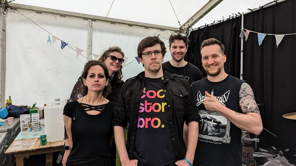 Chris and his bandmates backstage at a festival. Everyone is wearing black t-shirts and looking alternately grim and cheerful.