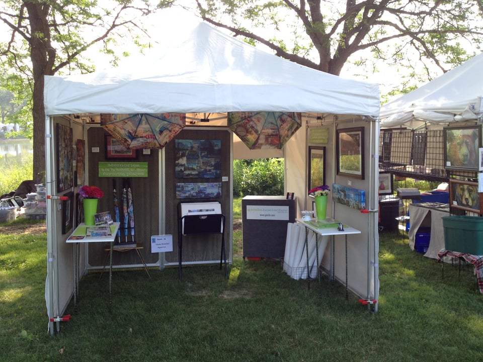 White tent at art fair on grass with displays of art inside.