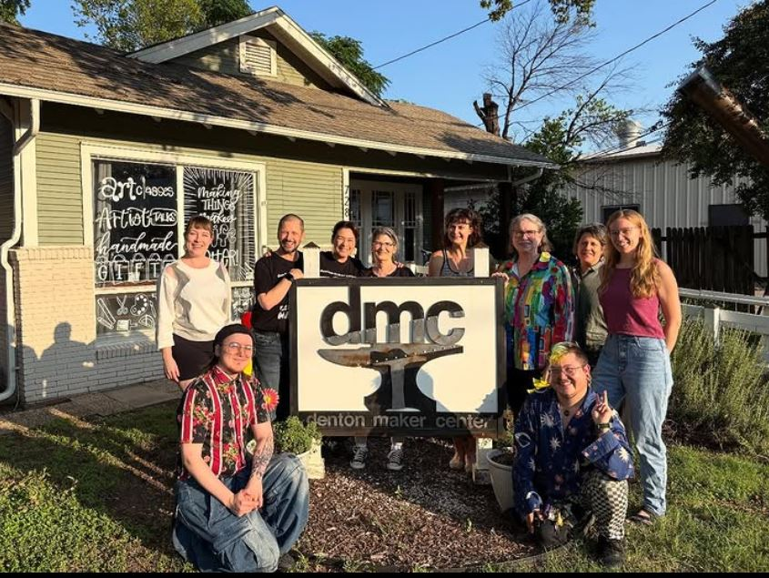 Denton Maker Center instructors all posed together in front of the sign.