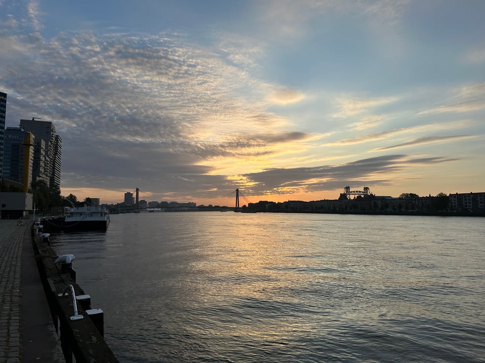 Photo of the Maas river separating north and south Rotterdam in early morning. There are sweeping clouds and the sun is reflecting on the undulating water
