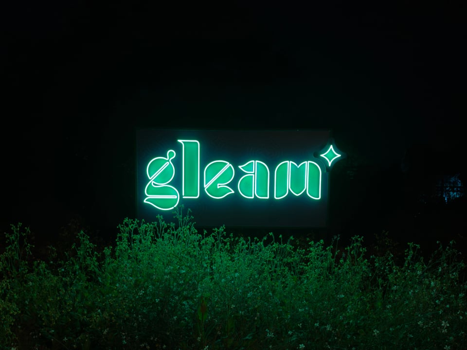 Night photo of LED sign above a hedge that says gleam.