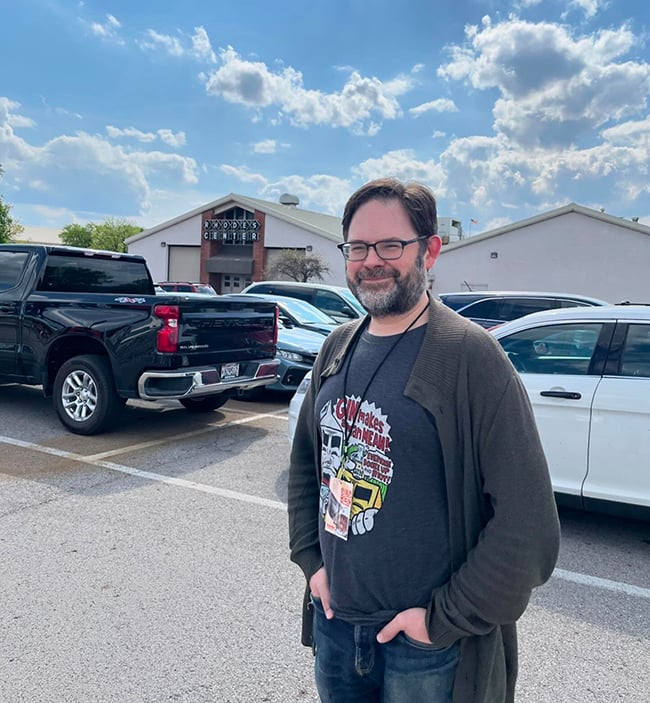A middle-aged cartoonist wearing a Milk & Cheese shirt standing in front of the Rhodes Center building in Columbus, Ohio.