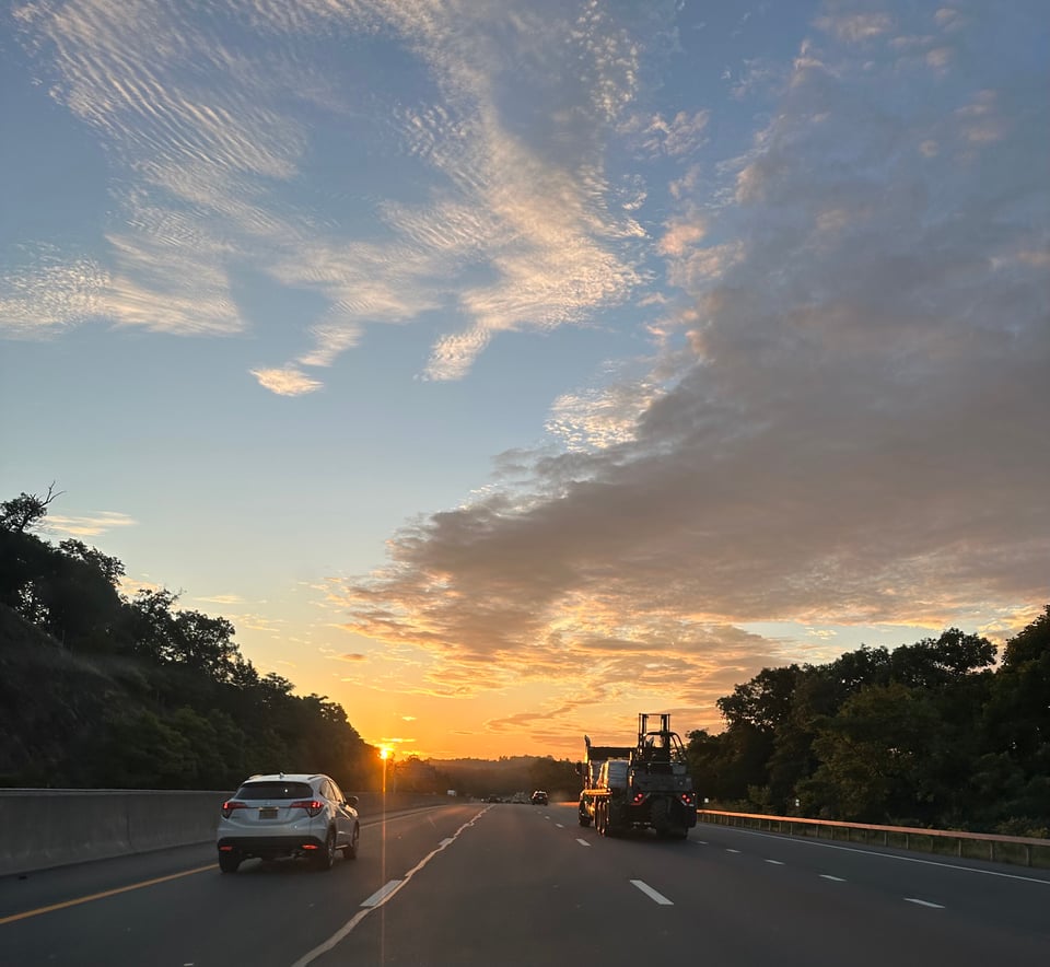 photo of sunrise from moving car on the NY Thruway; the clouds a gold and some are ridged