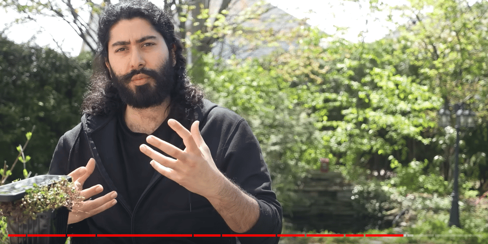 A still from a video with a bearded person looking at the camera