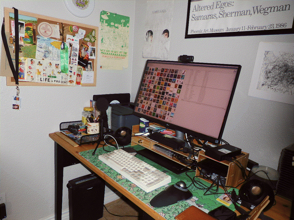 A computer desk surrounded by colorful clutter and memorabilia. The keyboard is beige and chunky, and there is a trackball-style pointing device next to it.