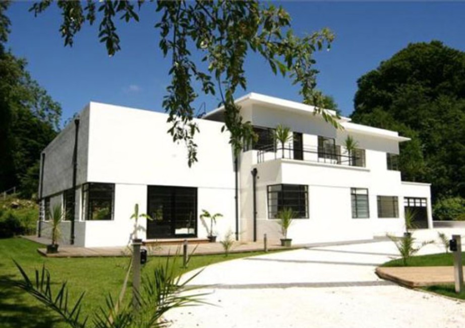 A white moderne house. It's several interlocked blocks, with a covered balcony above the hall and black critall style frames.