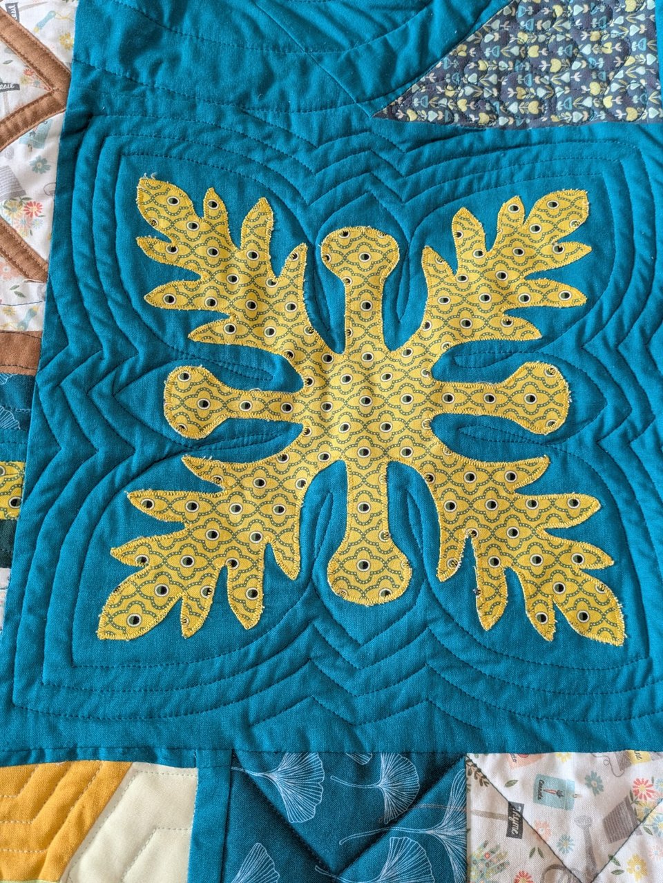 A patchwork quilt square in the Hawaiian tradition: sea blue with a radially symmetrical yellow-green leaf in the centre