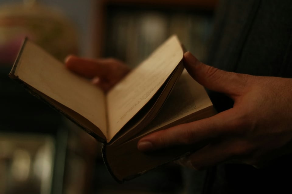 Two hands in dim light hold a book.