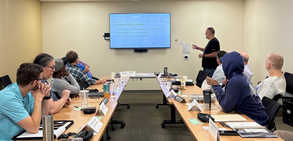 Chris explains a slide on the TV screen display that says Key Sales Points to Look For to a room of NRG members.