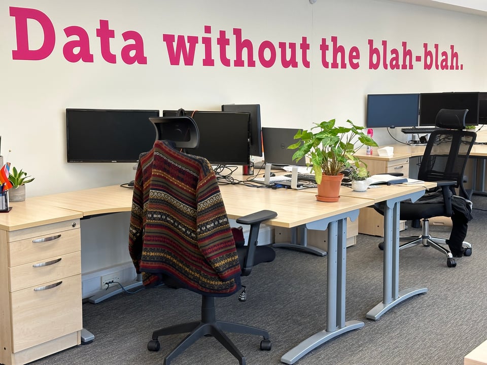 Photograph of an office interior: desks, chairs, computers. A large sign on the wall says,”Data without the blah-blah.”