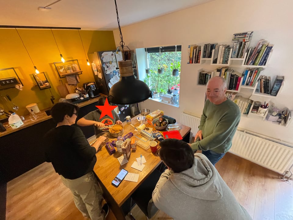 Four people are around the kitchen island as two of them work on making a chocotorta.