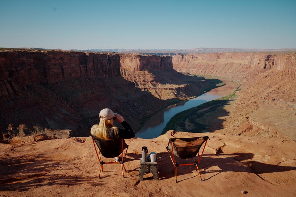 A woman in a camp chair overlooks a winding river in a canyon in Utah from above