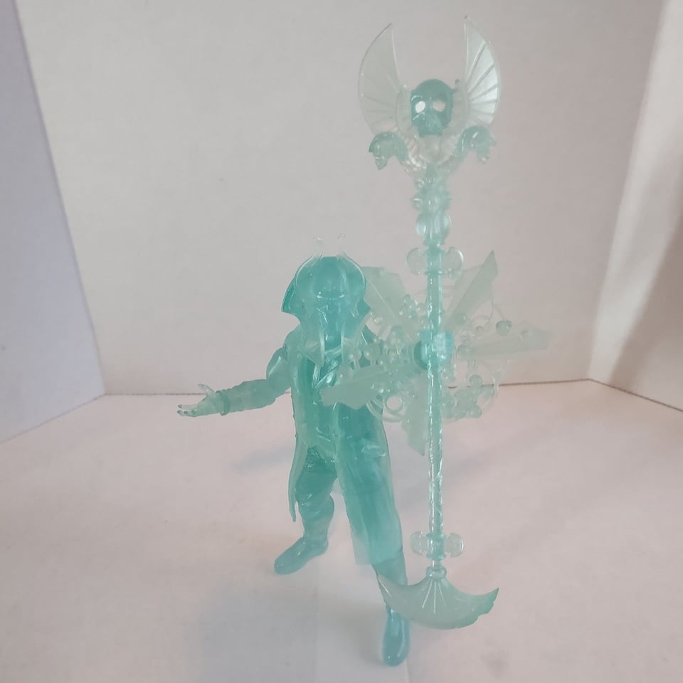 A translucent, sky blue action figure of a man in an elaborate Egyptian helmet/ headdress holding a staff decorated with a winged skull up into the air