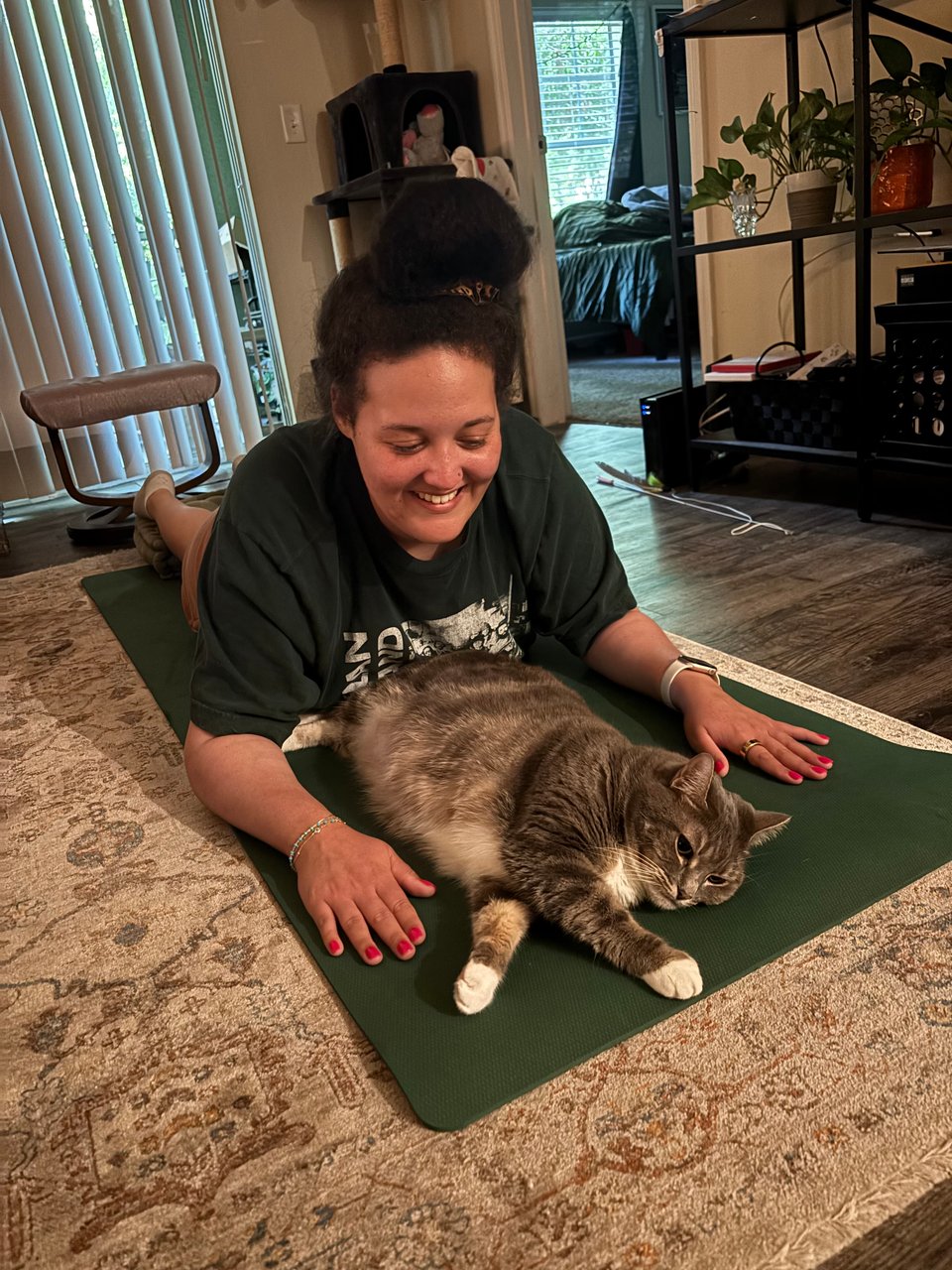 An image of Andrea laying down on a yoga mat with a gray cat laying between her arms.