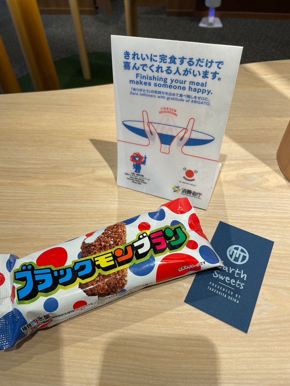 A packaged ice cream, a card reading Earth Sweets (the name of the restaurant), and a sign that encourages you to leave no food waste.