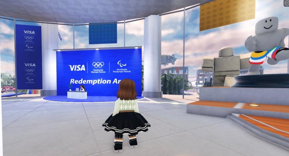 Roblox screenshot of a character standing in front of a desk labelled "Redemption Area", with the Visa and Olympic logos