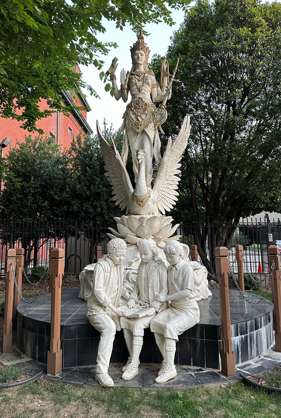 Photo of Hindu god Dewi Saraswati statue in Washington, DC. She is standing on swan standing on a lotus, with three young students at her feet