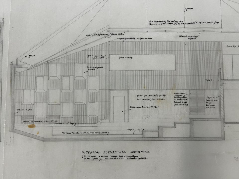 A detailed drawing of the southern internal elevation of the council chamber. The drawing shows the shape of the chamber, which is roughly an oblong with the leftmost corners removed. A set of squarish windows are set in a checkerboard pattern at one end, whilst the rest is wood paneling.