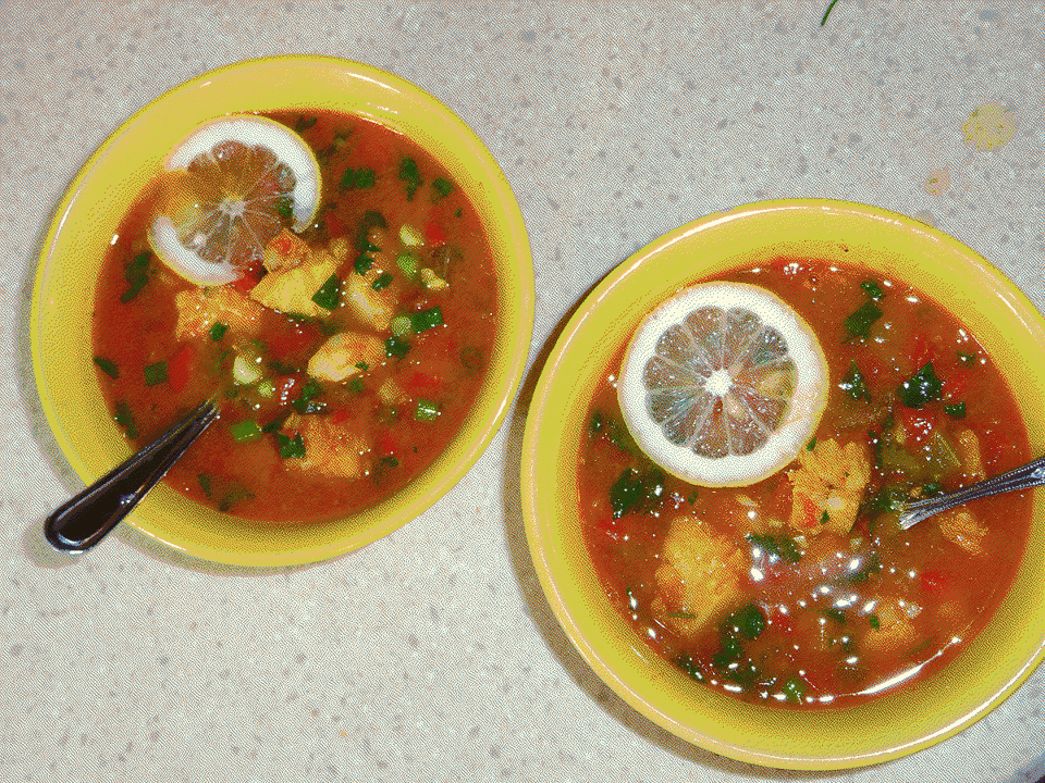 Two bowls of soup with fish and veggies topped with thin slices of lemon.