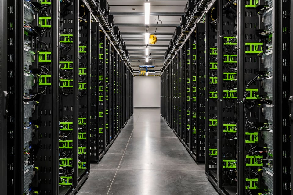image of an aisle of a data center with several rows of black computer servers with wires