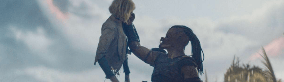 A screenshot from Predator: Badlands. A barefaced predator holds half an android aloft. She seems fine with it.