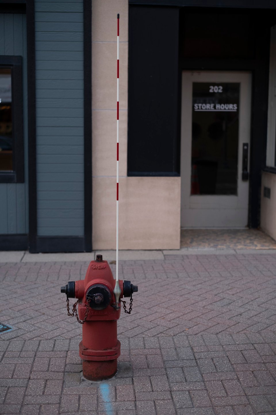 A fire hydrant on a brick sidewalk with a red and white stick extending upwards from the side.