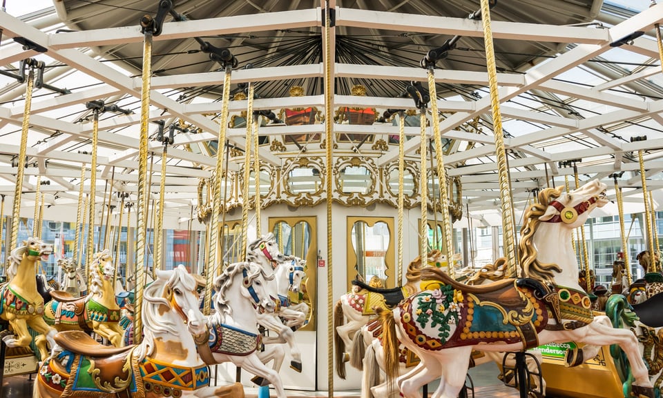 The inside of the LeRoy King Carousel with a number of horse figures and chariots.