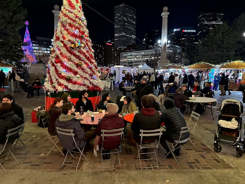 A lot of people talking about a book near a Christmas tree.