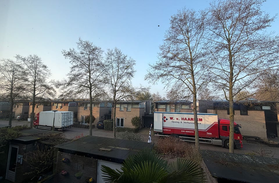 Two moving trucks preparing to empty out a house on a street in the early morning.